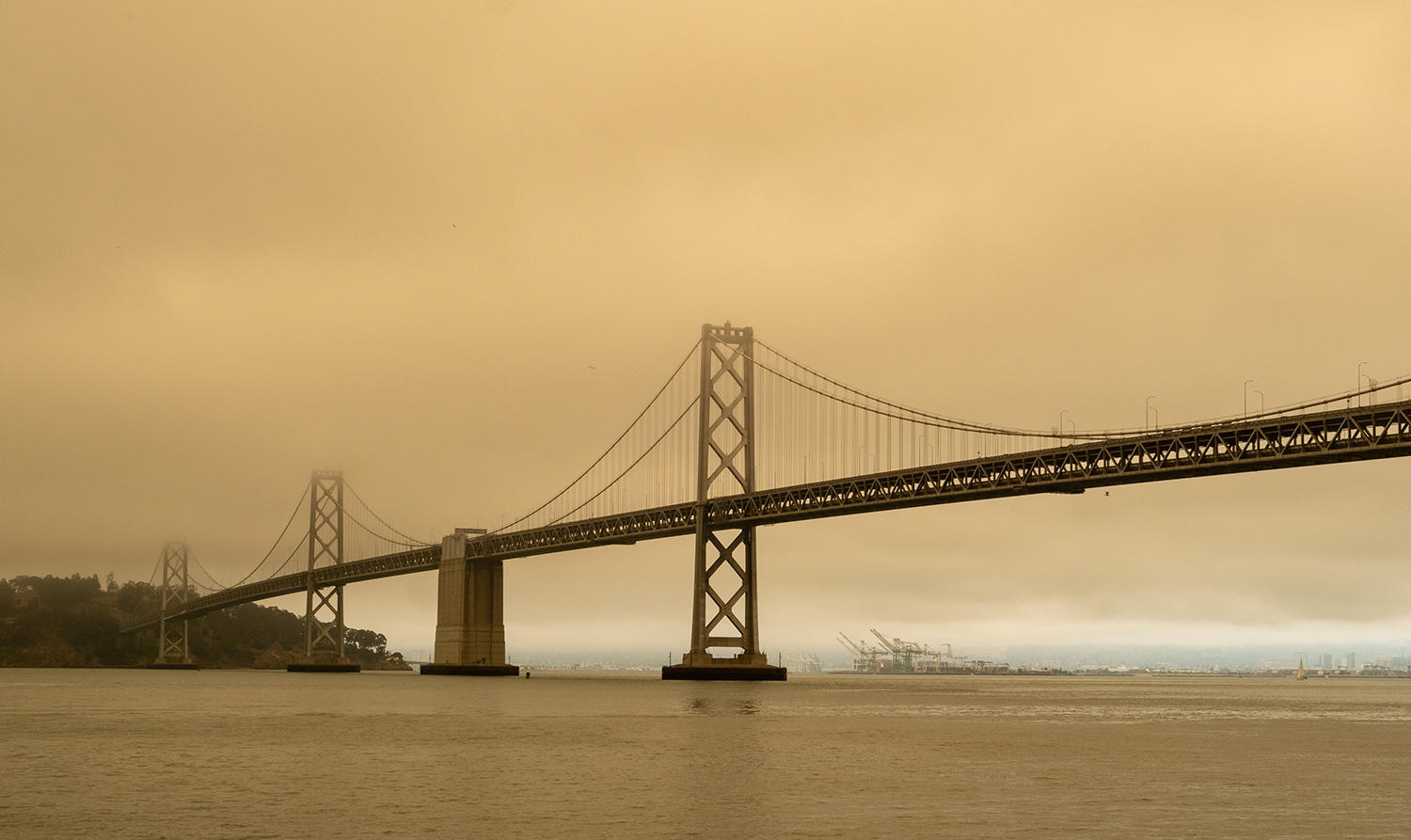 SAN FRANCISCO, CA JULY 1, 2018: Bay Bridge surrounded by smog by nearby wildfires. Clean air can be seen in the distance at the Port of Oakland